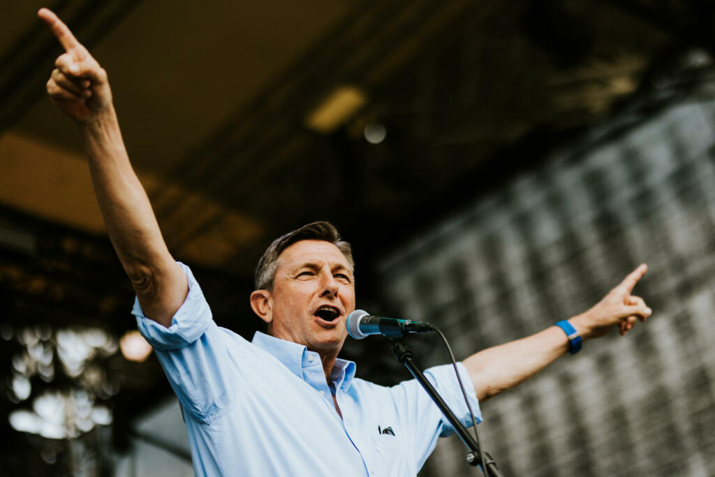 Borut Pahor z dvignjenimi rokami pred mikrofonom