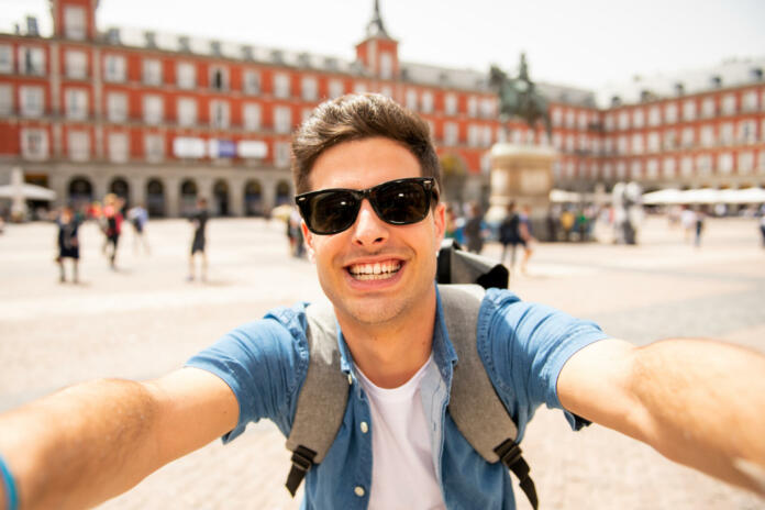 Attractive young caucasian tourist student man having fun happy and excited taking a selfie with smart phone in Plaza Mayor, Madrid, Spain. Travel,vacation, holidays in European city concept.