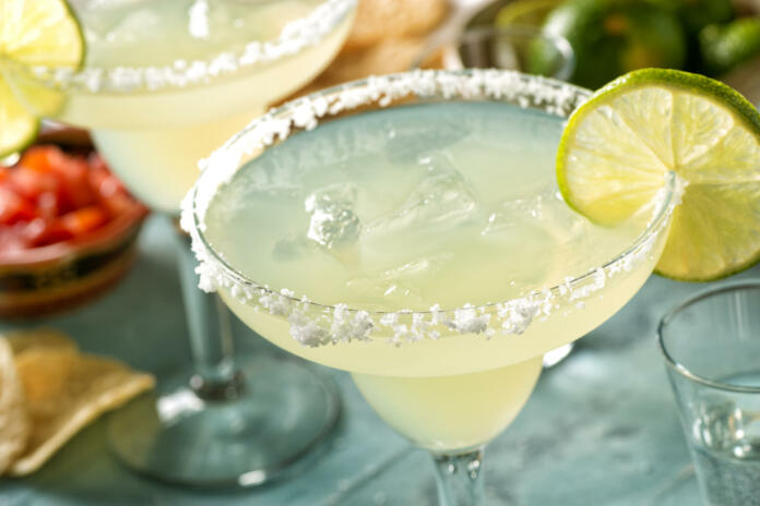 Delicious tequila and lime margaritas on an outdoor table with tortilla chips and pico de gallo.