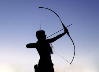Predzgodovinske ženske so bile lovke in umetnice, ne samo matere Female ginger hair archer shooting targets with her bow and arrow. Concentration, target, success concept. Copy space text.