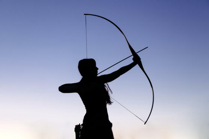 Female ginger hair archer shooting targets with her bow and arrow. Concentration, target, success concept. Copy space text.