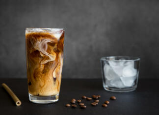 Osvežilni kavni napitki za vroče poletne dni Iced coffee in tall glass with cream, container with ice, cocktail straw and coffee beans on dark background with copy space. Refreshing drink.