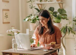5 korakov za dokončanje diplome Positive young mixed race woman using a laptop and smartphone at home.Cozy home interior with indoor plants.Remote work, business,freelance,online shopping,e-learning,urban jungle concept.