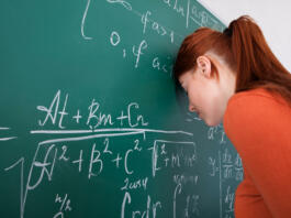 Side view of sad young female student leaning head on blackboard in classroom