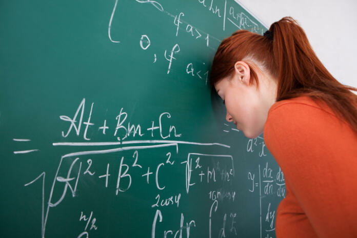 Side view of sad young female student leaning head on blackboard in classroom