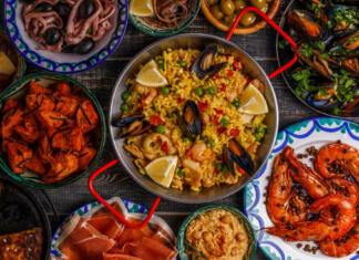 Top 10 najpopularnejših jedi na svetu Typical spanish tapas concept. Concept include slices jamon, bowls with olives, anchovies, spicy potatoes, mashed chickpeas, shrimp, calamari, manchego with quince marmalade, pans with tortilla, paella, mussels on a wooden table.