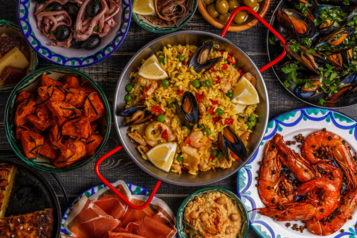 Typical spanish tapas concept. Concept include slices jamon, bowls with olives,  anchovies, spicy potatoes, mashed chickpeas, shrimp, calamari, manchego with quince marmalade, pans with tortilla, paella, mussels  on a wooden table.