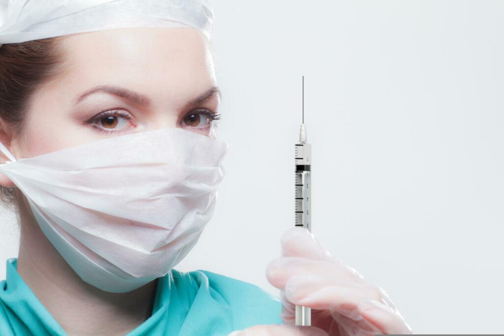 Zdravnica z belo masko v roki drži injekcijsko iglo