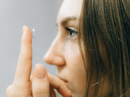 Ženska na prstu pred obrazom drži kontaktne leče