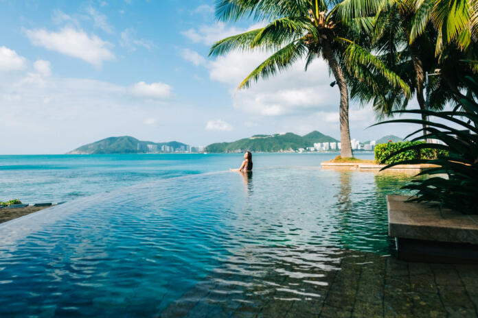 Young caucasian woman in swimming pool on beautiful tropical bay, blue sky and ocean, summer vacation concept.