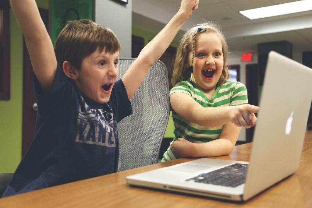 Deček in deklica navdušeno igrata igrice na prenosnem računalniku