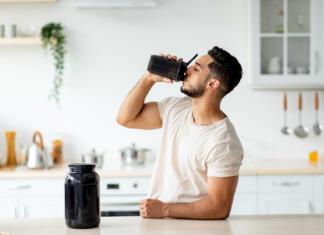 Prehranska dopolnila Young Arab guy drinking protein shake from bottle at kitchen, copy space. Millennial Eastern man using meal replacement for weight loss, having sports supplement for muscle gain. Body care concept