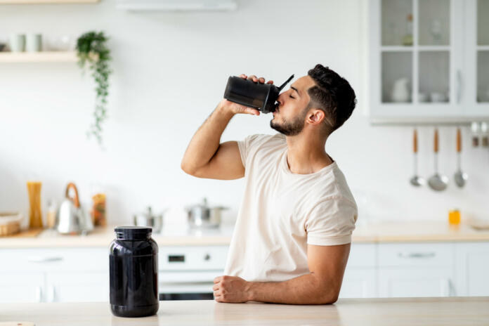 Young Arab guy drinking protein shake from bottle at kitchen, copy space. Millennial Eastern man using meal replacement for weight loss, having sports supplement for muscle gain. Body care concept