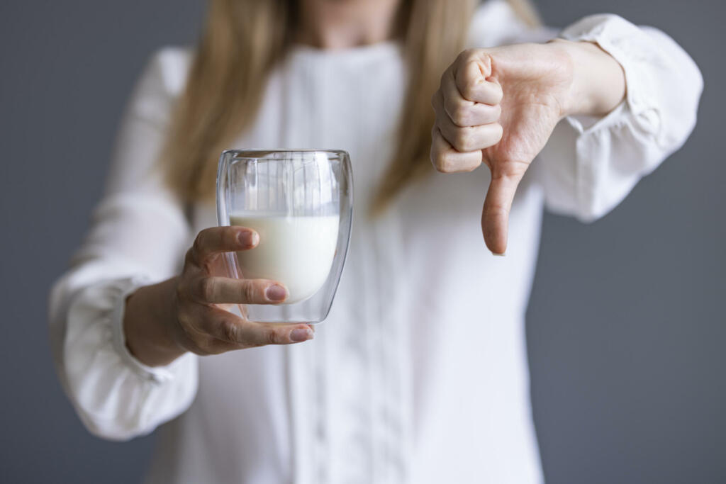 Ženska v eni roki drži kozarec mleka, v drugem pa navzdol obrnjen palec