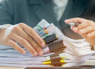 Uredite si tudi dopolnilno zdravstveno zavarovanje Accounting planning budget concept : Business woman offices working for arranging documents unfinished stack of document papers with pen, calculator, clip papers on busy office desk