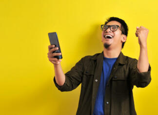Brezplačno do USB ključa 8GB! Asian man holding smartphone with winning gesture. Asian bussinesman winning gift or lottery, on yellow background