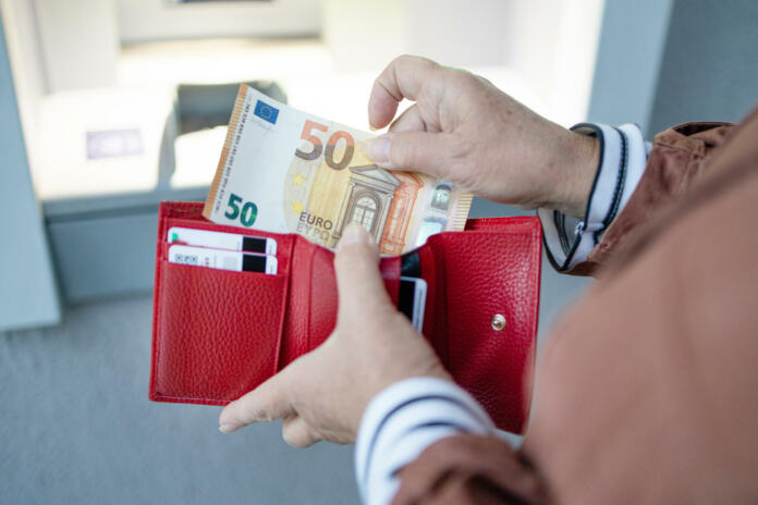 ATM machine and euros cash. Closeup of woman hand holding euro banknotes. Withdraw money from an ATM