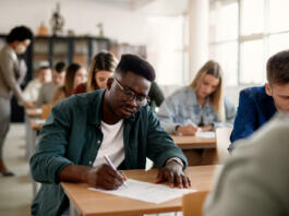 Black male student and his classmates writing during exam at the university.