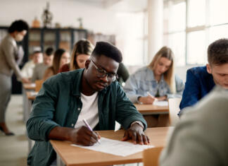 Matura: kje, kaj, kako, zakaj … Black male student and his classmates writing during exam at the university.