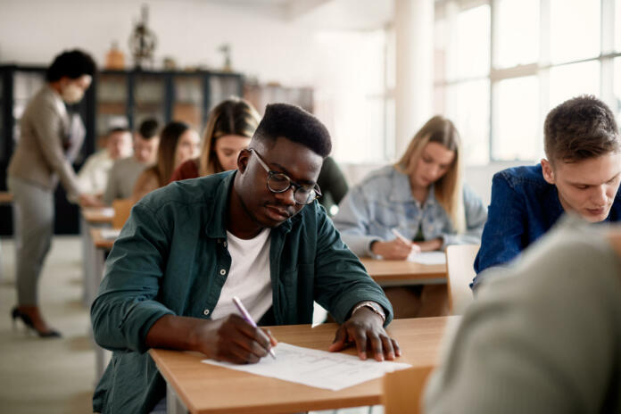 Black male student and his classmates writing during exam at the university.