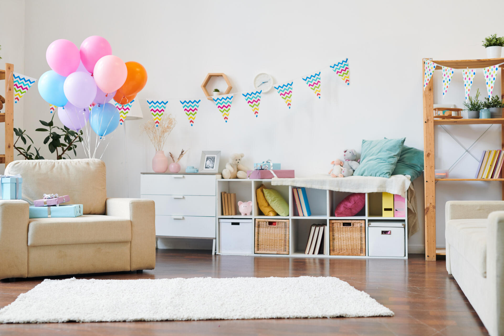 Bunch of colorful balloons and stack of giftboxes on armchair in the living-room decorated with flags for home birthday party