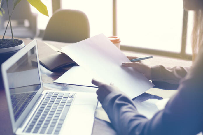 Businesswoman with documents paper sheet in loft modern office, working on laptop computer. Team working, business people. Space for design layout