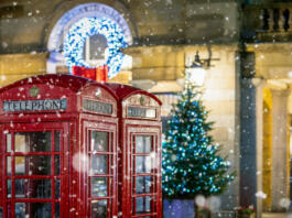 Classic, red telephone booths with snow falling in front of Christmas decorations lights in the Covent Garden area, London, United Kingdom