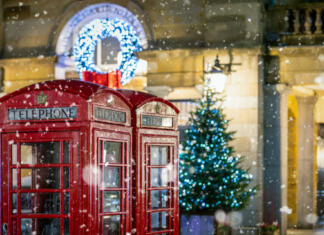 Praznovanje božiča po svetu Classic, red telephone booths with snow falling in front of Christmas decorations lights in the Covent Garden area, London, United Kingdom
