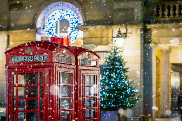 Classic, red telephone booths with snow falling in front of Christmas decorations lights in the Covent Garden area, London, United Kingdom