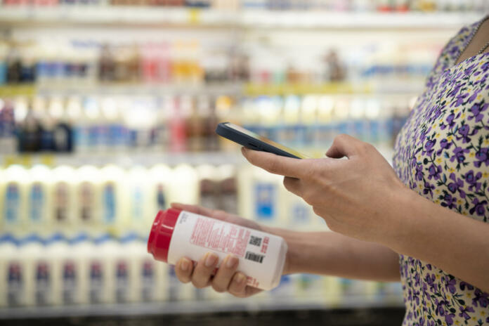 close up of asian young businesswoman is shopping for meat and scanning barcode with smart phone at supermarket