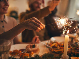 Close up of hand holding sparkler over Christmas dinner background, copy space