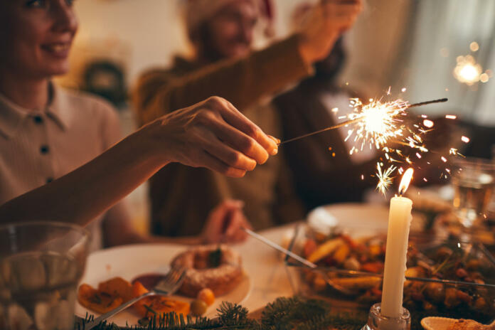 Close up of hand holding sparkler over Christmas dinner background, copy space