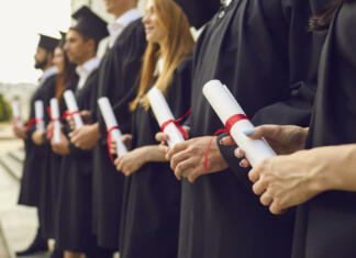 Podaljšanje absolventa Close up of row of students in black robes standing with traditional rolled up diplomas in hands at graduation ceremony. Happy graduates with honors in black togas celebrating their milestone event
