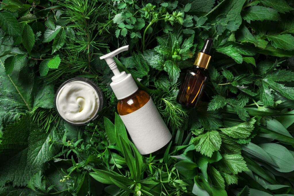 Cosmetic skin care products (body lotion, hair shampoo, face creme, essencial oil, serum) on green leaves as background, top view. Natural eco beauty and organic green skin care concept.