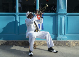 Kuba – konec romantike Cuban musician playing the trumpet next to a cuban flag at a street in Old Havana
