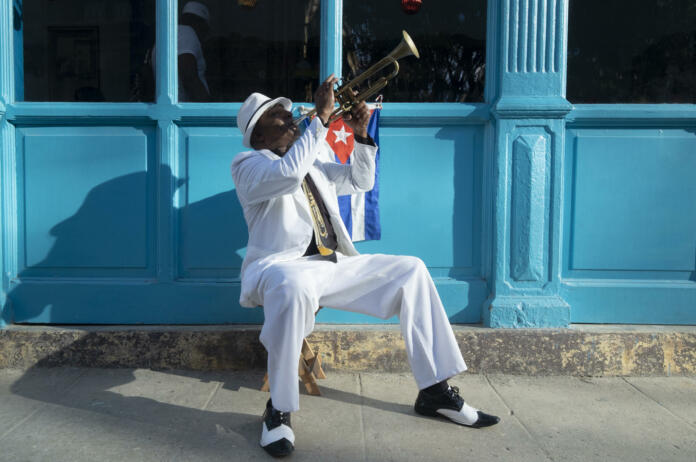 Cuban musician playing the trumpet next to a cuban flag at a street in Old Havana