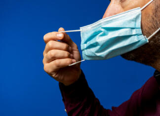 Se vračajo maske? Posvetovalna skupina odgovarja Detail of face of hispanic man taking off his surgical mask isolated on blue background, he gets rid of the mask astied from the desperate situation of the new normal caused by the coronavirus.