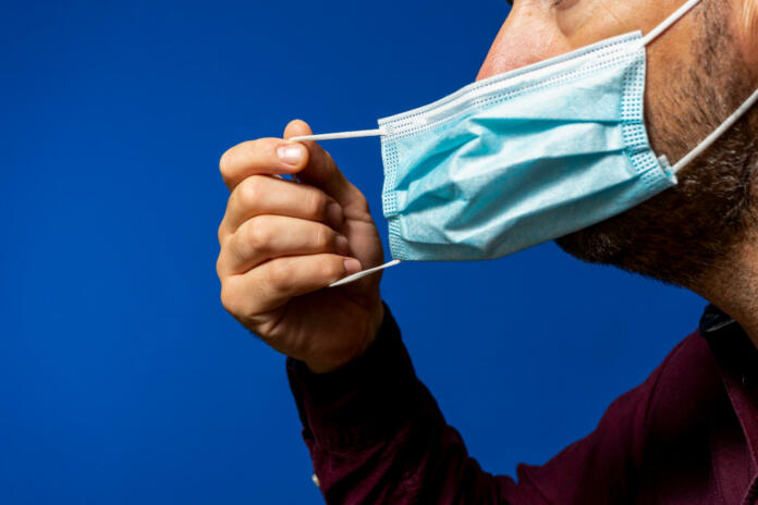 Detail of face of hispanic man taking off his surgical mask isolated on blue background, he gets rid of the mask astied from the desperate situation of the new normal caused by the coronavirus.