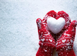 Skrivnostni čar »veselega decembra« Female hands in knitted mittens with snowy heart against snow background. Love, winter and Valentines day romantic creative concept with copy space for text
