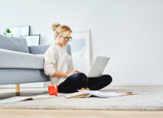 Iščem, iščem … streho nad glavo Female student sitting on floor of her apartment with laptop and notes studying