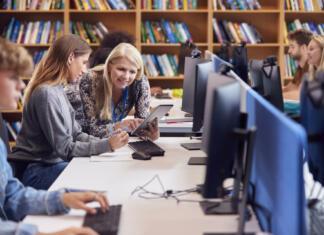 Kako šole skrbijo za dijake z učnimi težavami? Female University Or College Student Working At Computer In Library Being Helped By Tutor