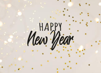 Kako se reče srečno novo leto po… Festive gold background with Happy New Year celebration. Shining stars confetti and fairy lights on beige background. Flat lay, top view.