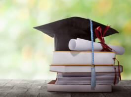 Graduation hat with degree paper on a stack of book against blurred background
