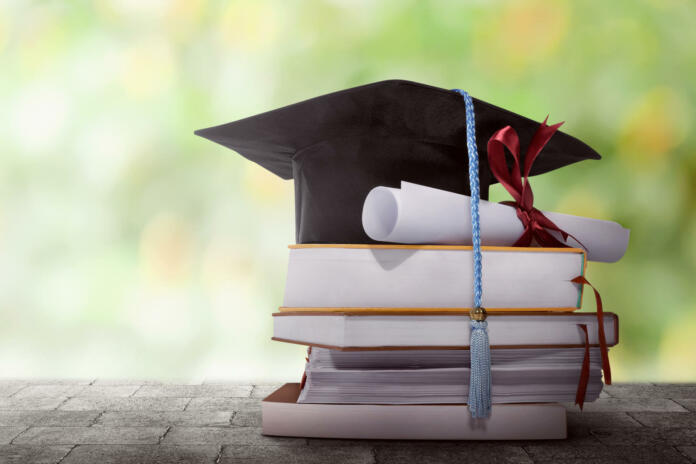 Graduation hat with degree paper on a stack of book against blurred background