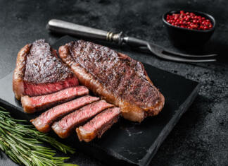 Neprestana utrujenost in brezvoljnost Grilled top sirloin or cup rump beef meat steak on marble board. Black background. Top view.