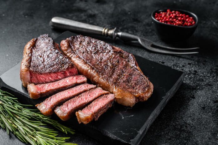 Grilled top sirloin or cup rump beef meat steak on marble board. Black background. Top view.