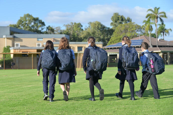 Group of Australian school students wearing school uniform walking together to school in the morning time.