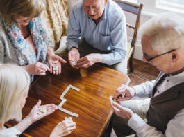 Group of senior friends are playing dominoes at a table together.