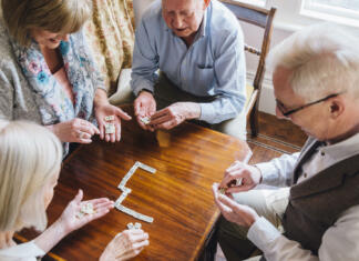 Družabne igre Group of senior friends are playing dominoes at a table together.