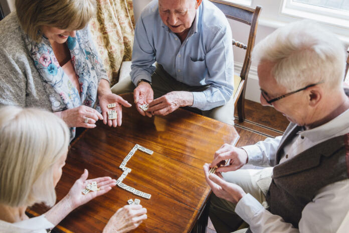 Group of senior friends are playing dominoes at a table together.